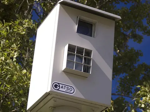 A white Gatso fixed speed camera housing on a pole