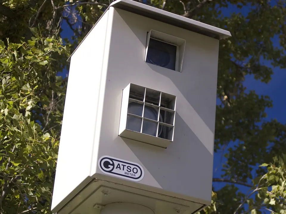 A white Gatso fixed speed camera housing on a pole
