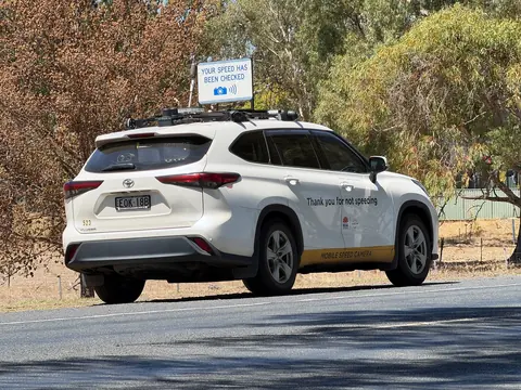 A white SUV with a raised roof sign saying your speed has been checked, parked at the roadside