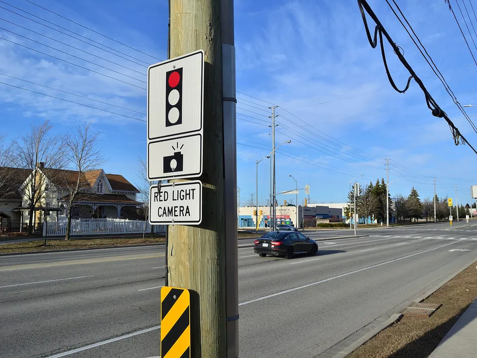 A red light camera sign on a pole at an intersection, with the camera beyond