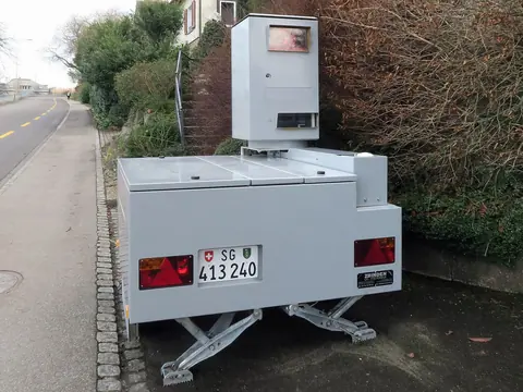 A white semi-stationary speed camera trailer parked on a pavement