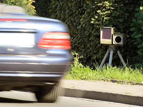 A mobile speed camera on a tripod at the kerb as a car passes