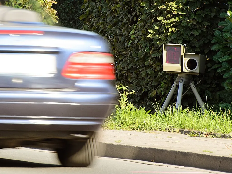 A mobile speed camera on a tripod at the kerb as a car passes