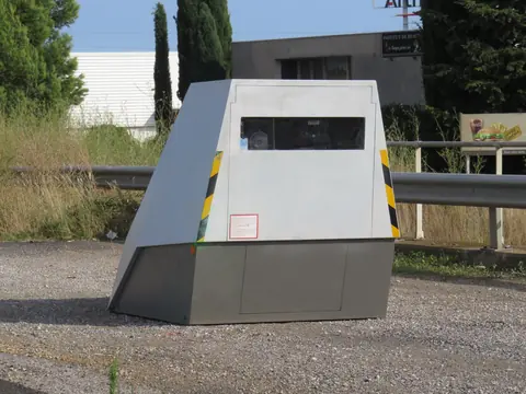 A grey movable speed camera cabin with yellow and black stripes at the roadside