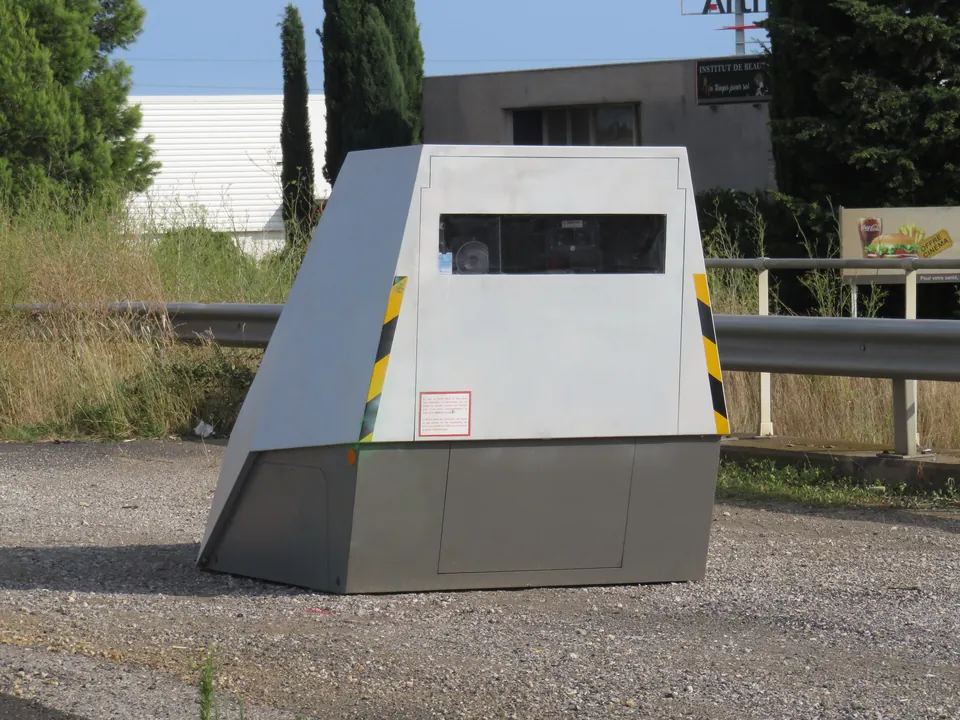 A grey movable speed camera cabin with yellow and black stripes at the roadside