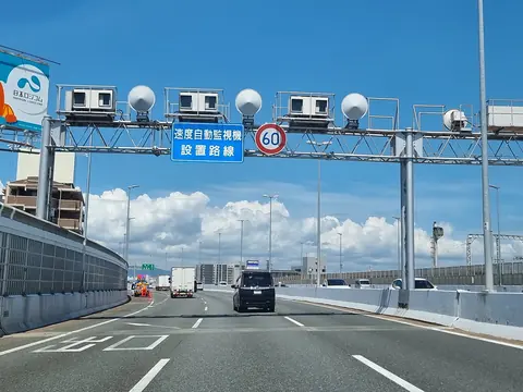 Speed cameras and flash units on a gantry over an expressway, with a sign saying speed is monitored automatically